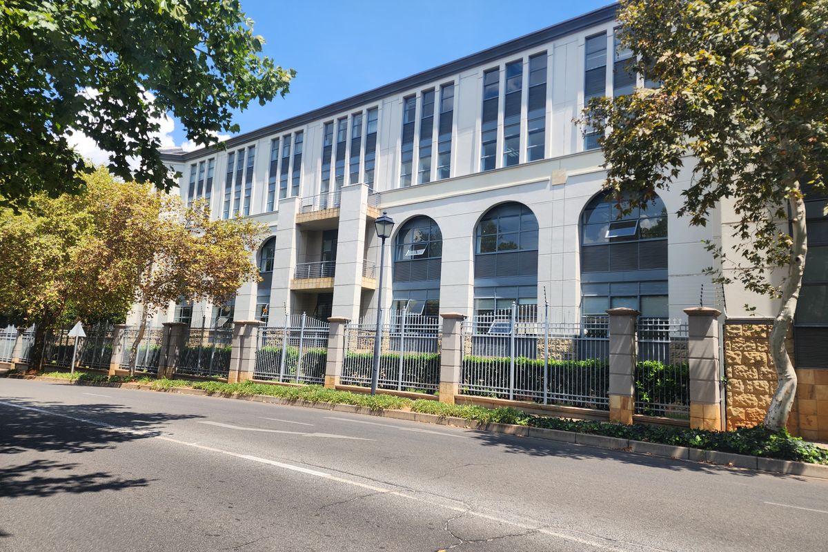A professional exterior view of a multi-story office building featuring arched windows, modern facade detailing, and secure perimeter fencing along the street.