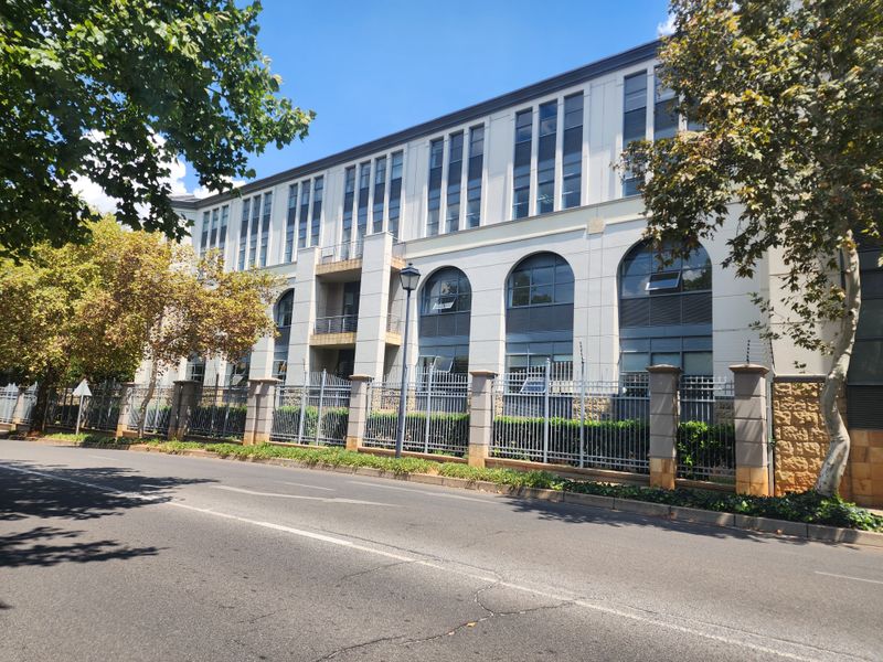 A professional exterior view of a multi-story office building featuring arched windows, modern facade detailing, and secure perimeter fencing along the street.