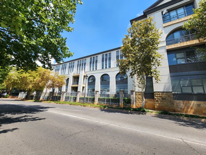 A well-maintained multi-story office building facade featuring arched windows, stone cladding, and secure perimeter fencing along the street front.