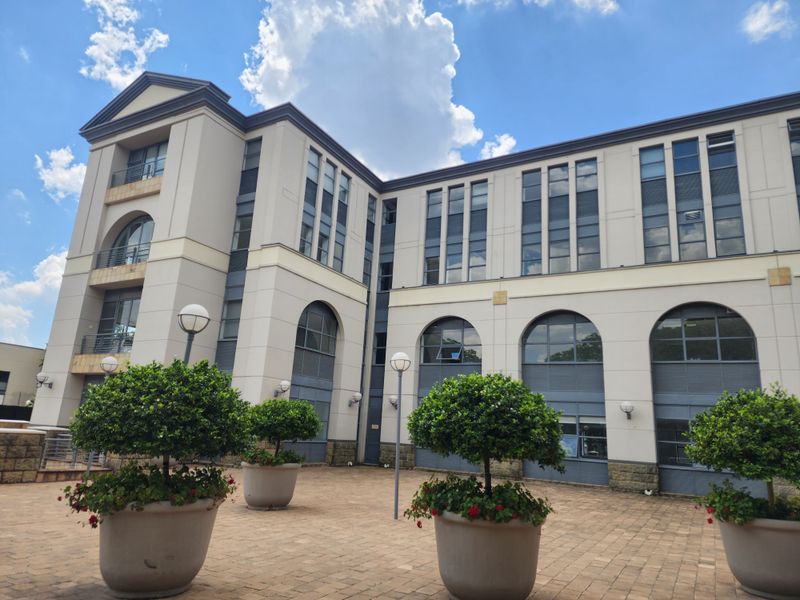 A well-maintained office building exterior featuring a paved courtyard, arched windows, and a modern multi-story facade.