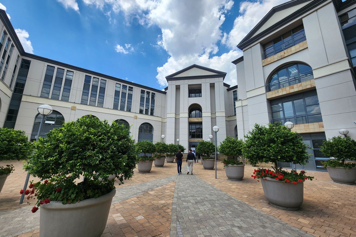 A well-maintained office complex courtyard featuring paved walkways, structured landscaping, and a multi-story building facade with classic architectural elements.