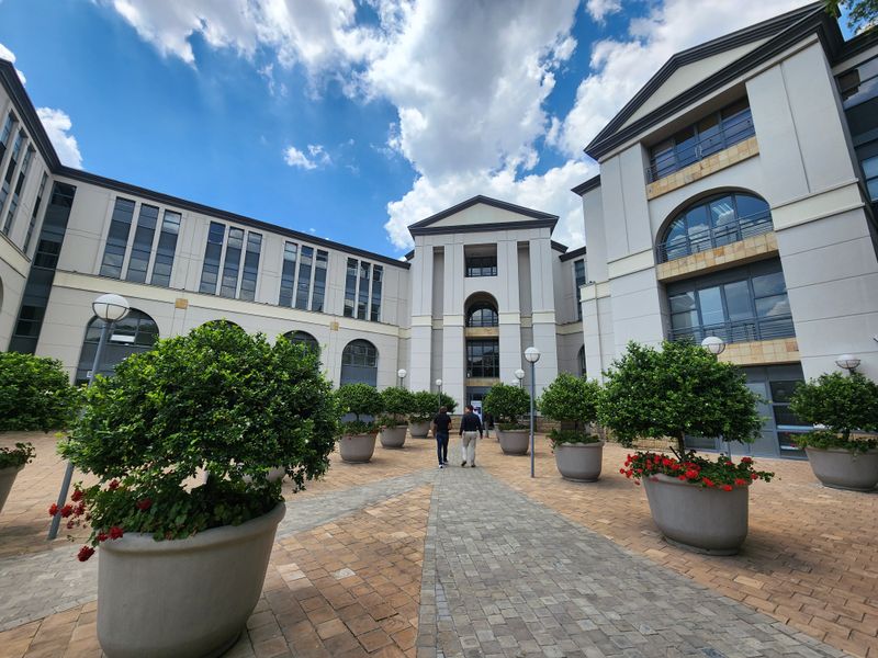 A well-maintained office complex courtyard featuring paved walkways, structured landscaping, and a multi-story building facade with classic architectural elements.