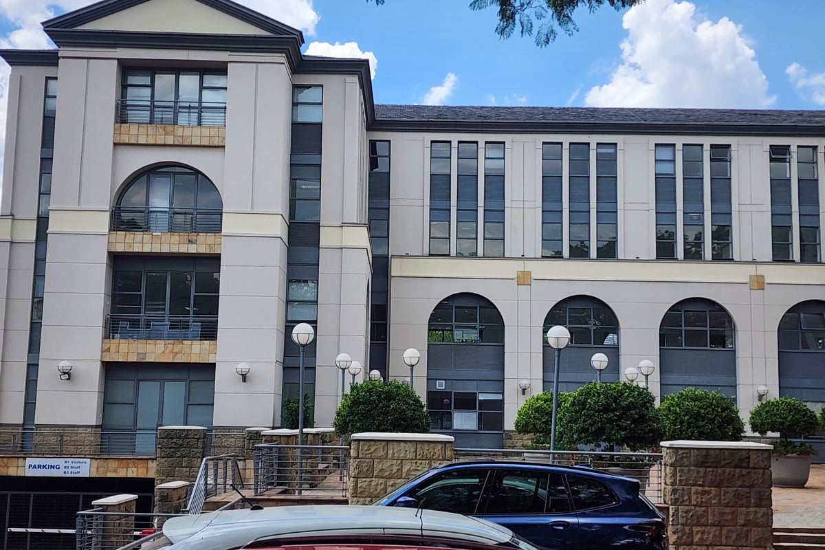 A multi-story office building facade featuring stone cladding, arched architectural details, balconies, and an integrated underground parking entrance.