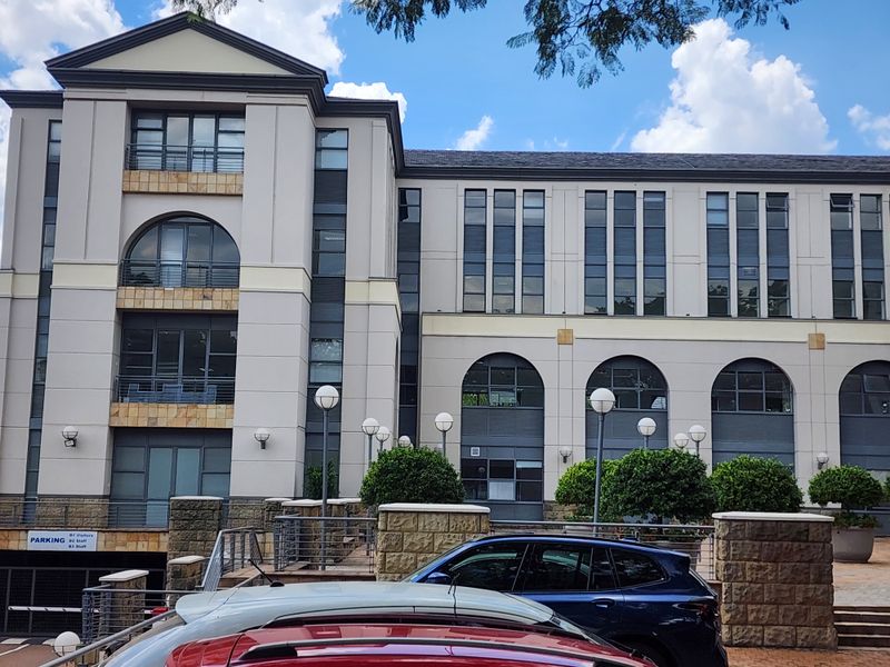 A multi-story office building facade featuring stone cladding, arched architectural details, balconies, and an integrated underground parking entrance.