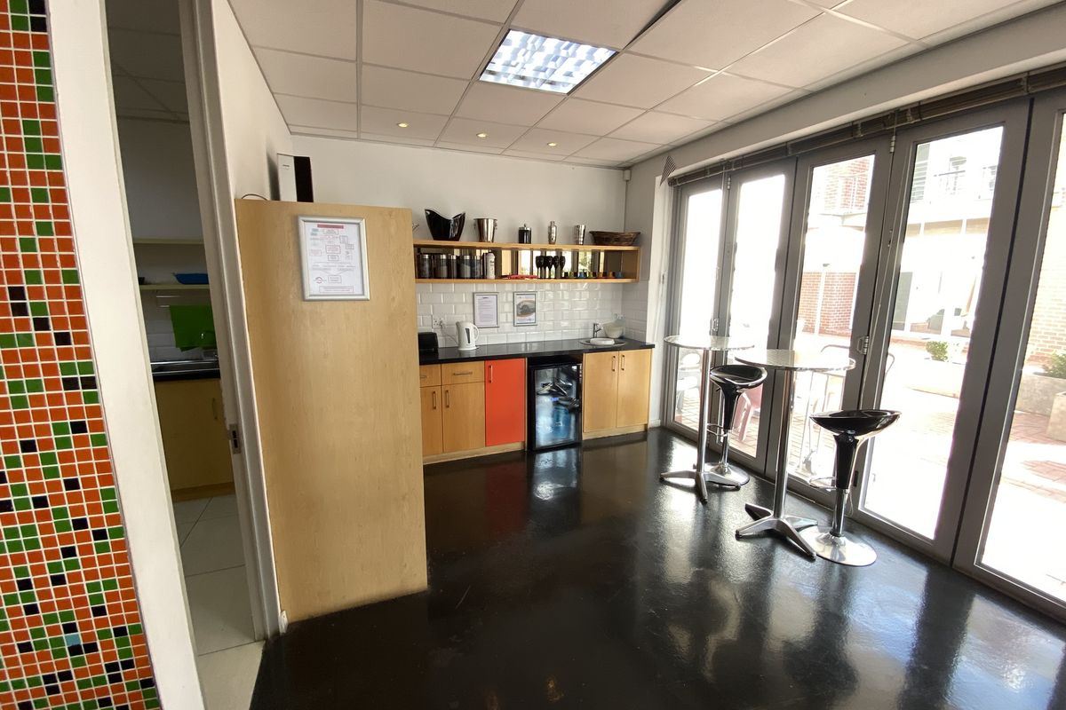 A functional office kitchenette featuring built-in cabinetry, a small under-counter fridge, and direct access to an outdoor patio through glass folding doors.