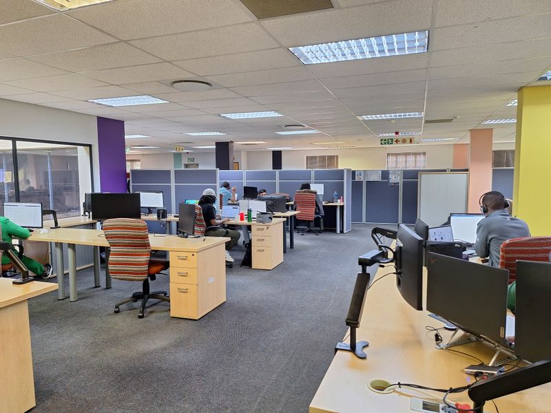 Open-plan office space featuring modular workstations, acoustic partition screens, suspended ceiling grid with integrated lighting, and carpeted flooring.