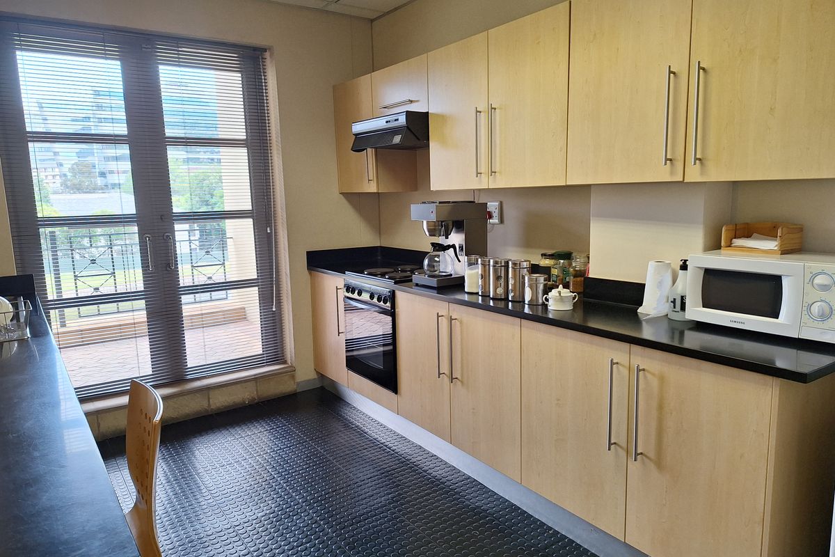 A functional office kitchenette featuring light wood cabinetry, black countertops, a built-in oven, and a glass door leading to a balcony.