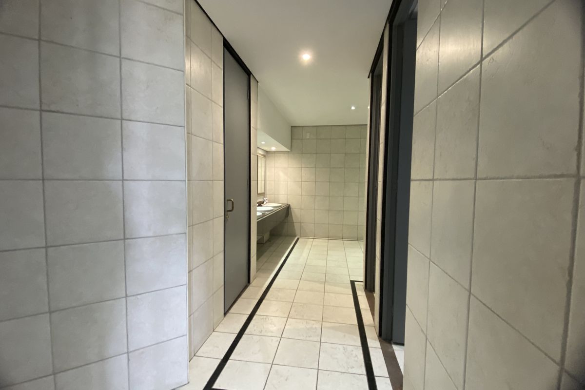 A clean, modern office restroom featuring tiled walls and flooring with a minimalist design and recessed lighting.