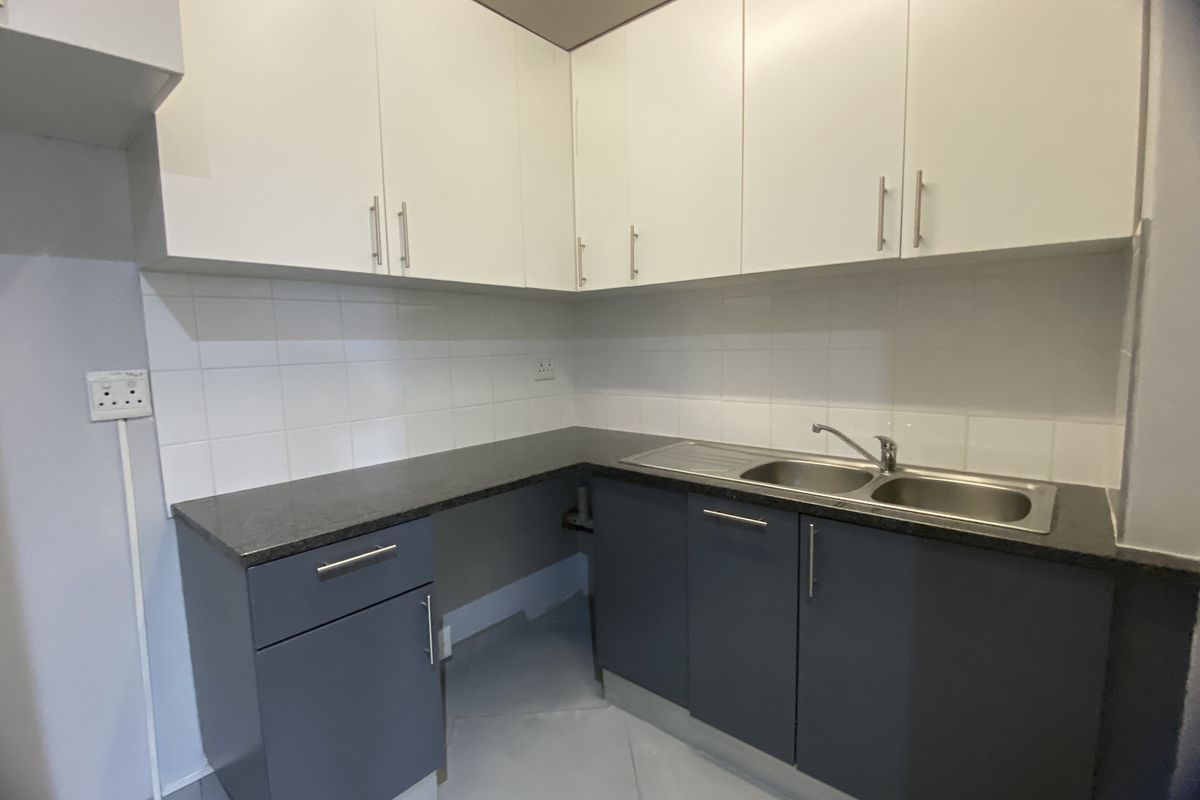 A compact kitchenette featuring modern two-tone cabinetry, dark stone-look countertops, a stainless steel double sink, and tiled splashbacks.