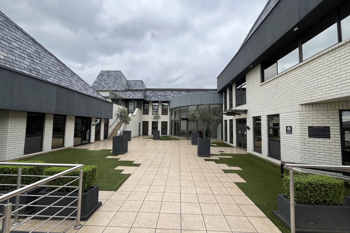A modern office courtyard featuring paved flooring, integrated artificial turf sections, and contemporary brick and slate building facades.