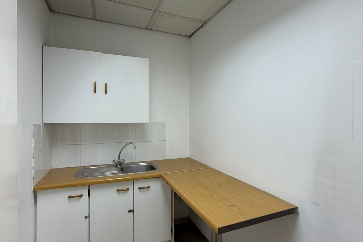 A small office kitchenette featuring basic white cabinetry, a stainless steel sink, laminate countertop, and a suspended ceiling with integrated lighting.