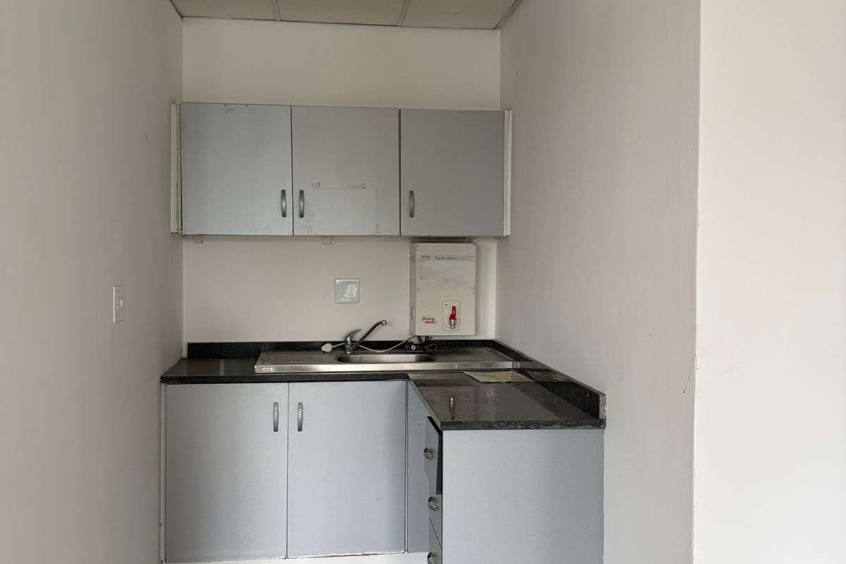 A small office kitchenette featuring built-in cabinetry, a stainless steel sink, and a wall-mounted water heater.