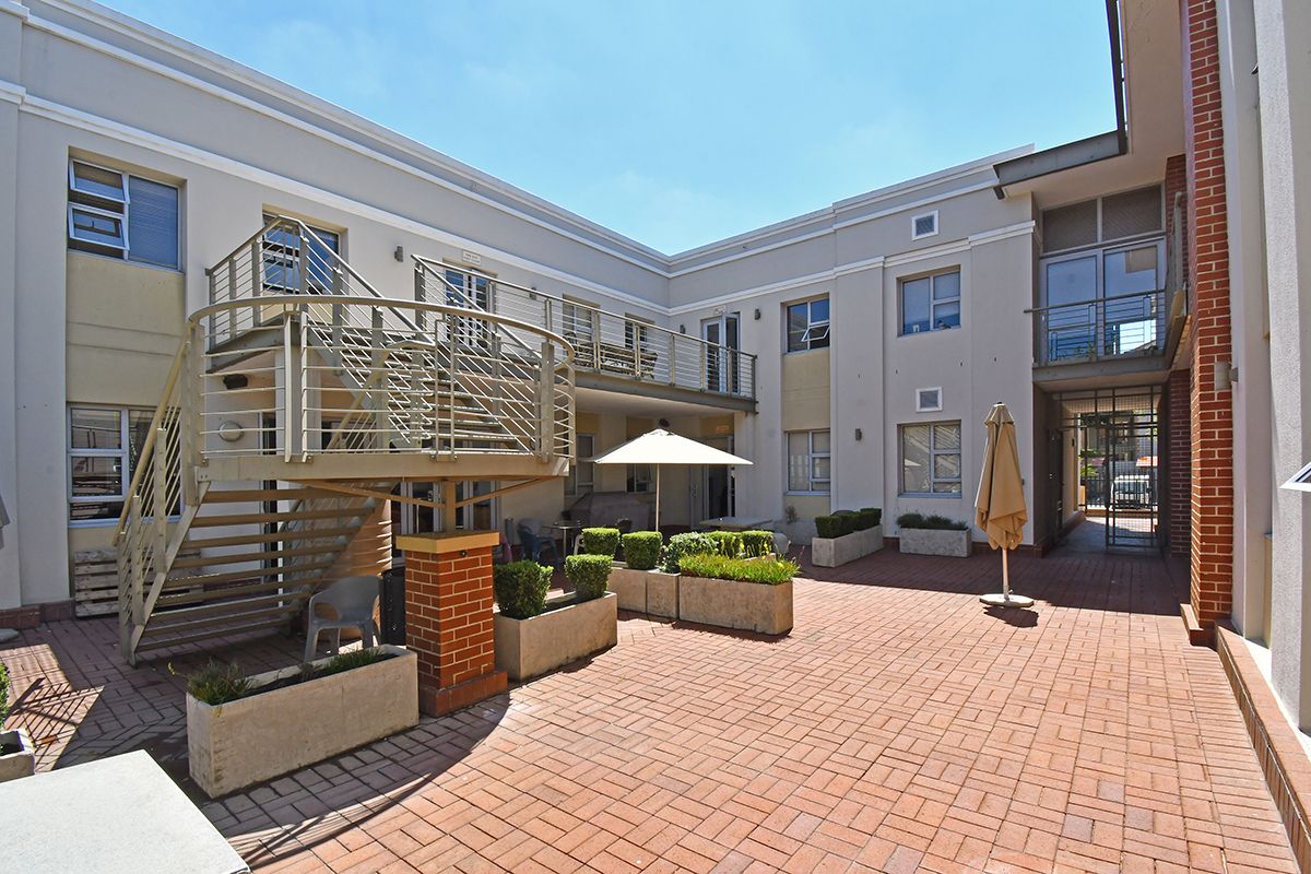 A paved courtyard area featuring a spiral metal staircase, integrated concrete planters, and access to the surrounding office building levels.