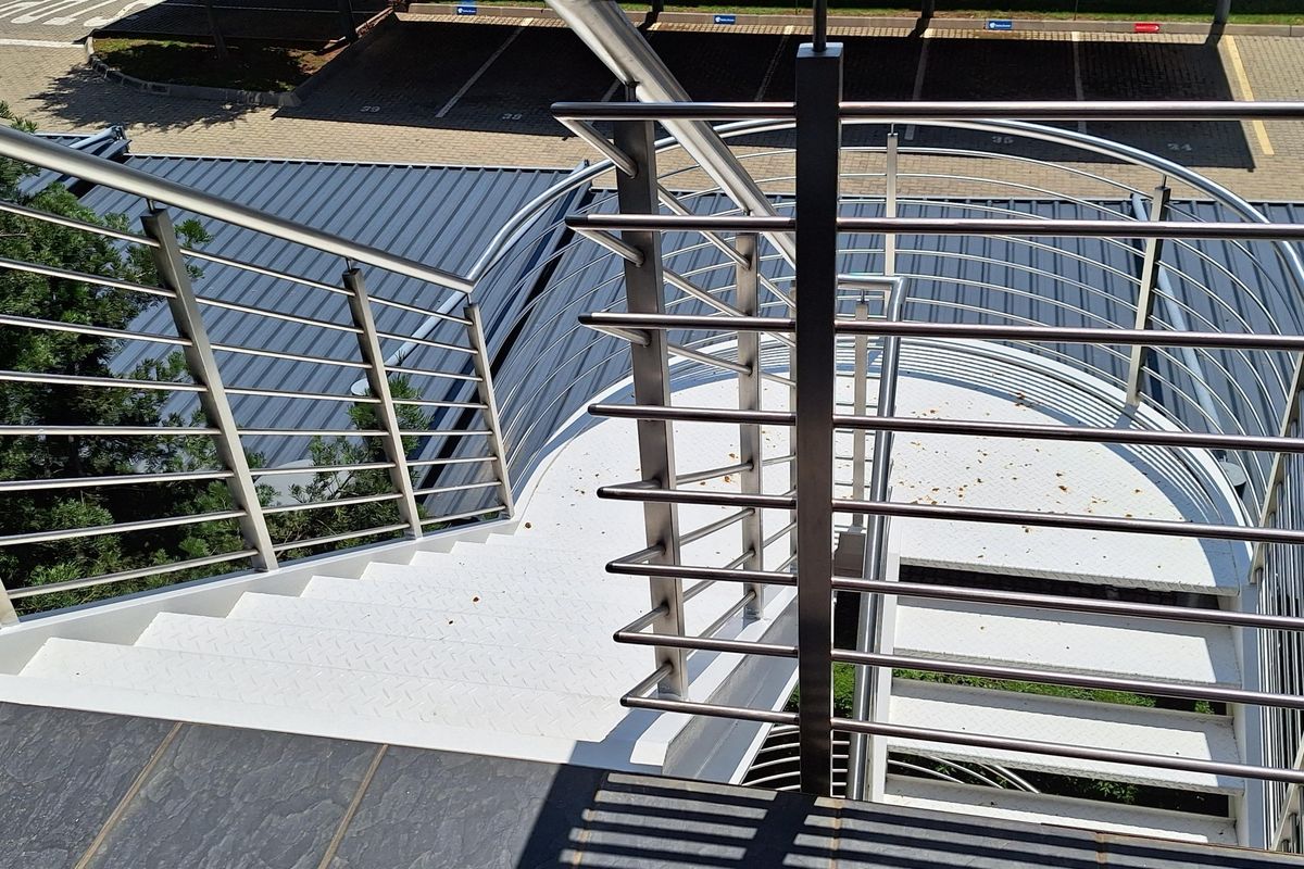 An elevated view of an external metal staircase with stainless steel railings, providing access to the office building exterior.