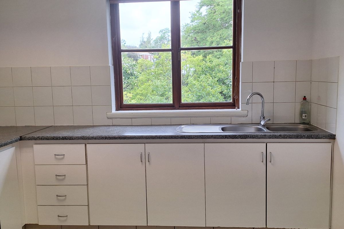 A functional office kitchenette featuring white cabinetry, a granite-look countertop, a stainless steel sink, and tiled splashbacks with a window view.