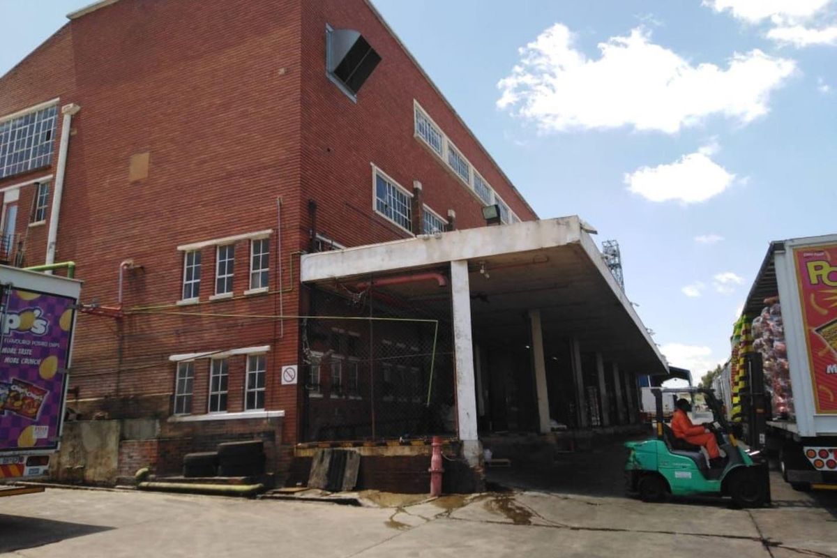 Industrial rear exterior view featuring a large brick warehouse building with a covered loading dock area and concrete apron.