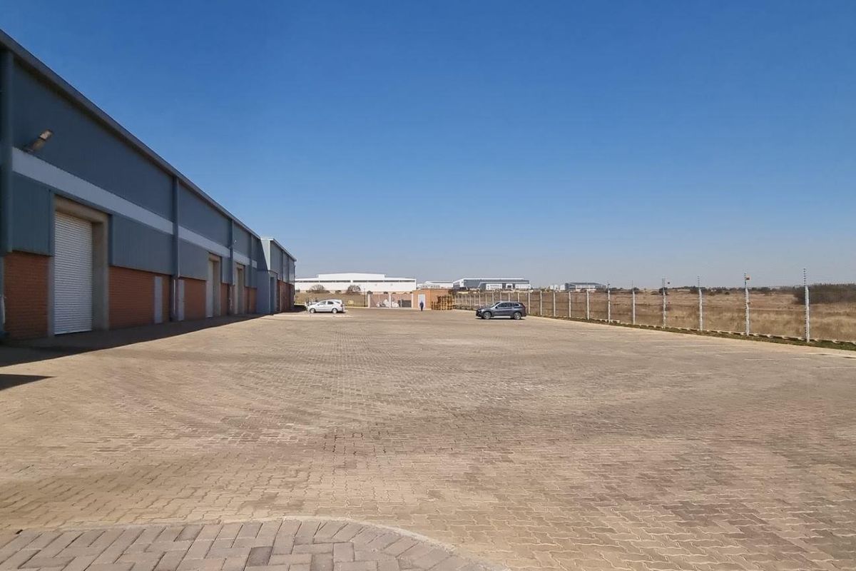 Spacious industrial yard featuring paved surface, multiple roller shutter doors, and secure perimeter fencing, ideal for logistics or storage operations.