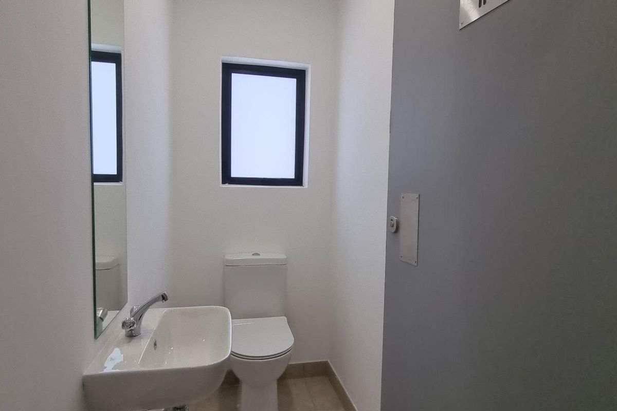 A clean, functional industrial restroom featuring a modern wall-mounted basin, a standard toilet, and a privacy window.
