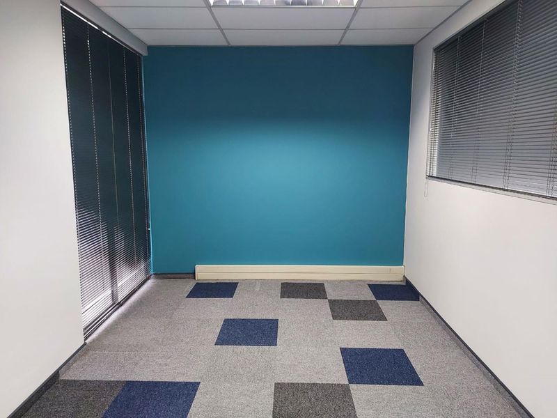 A clean, empty office space featuring carpet tiles, recessed ceiling lighting, and venetian blinds, ready for professional use.