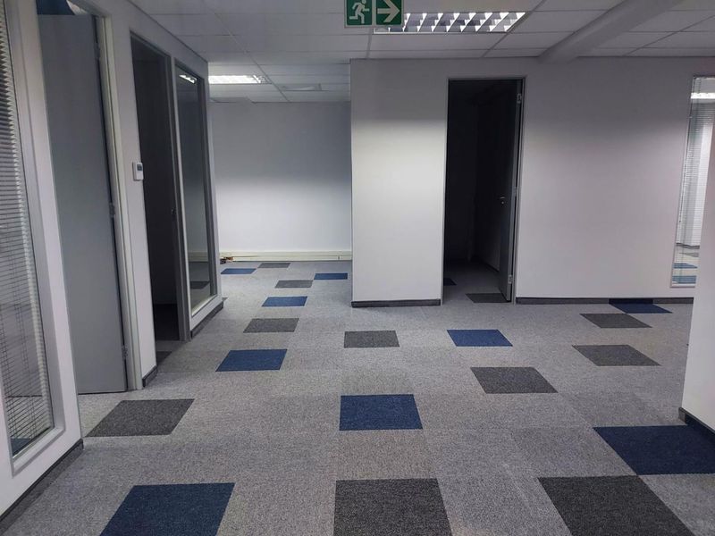 An empty office space featuring modern carpet tiles, glass partition doors, and a suspended ceiling with recessed lighting.