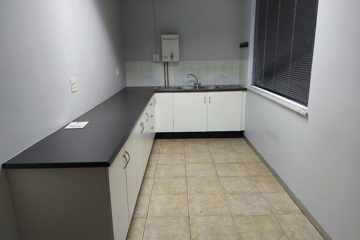 A functional office kitchenette featuring white cabinetry, dark laminate countertops, a stainless steel sink, and tiled flooring.