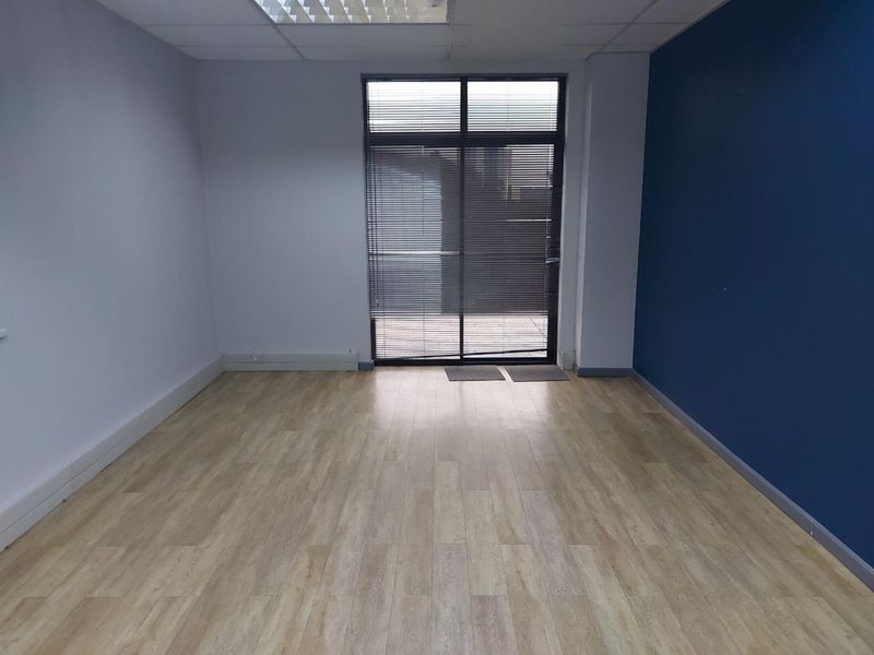 A bright, empty office space featuring laminate flooring, a suspended ceiling with recessed lighting, and a glass door with integrated blinds.