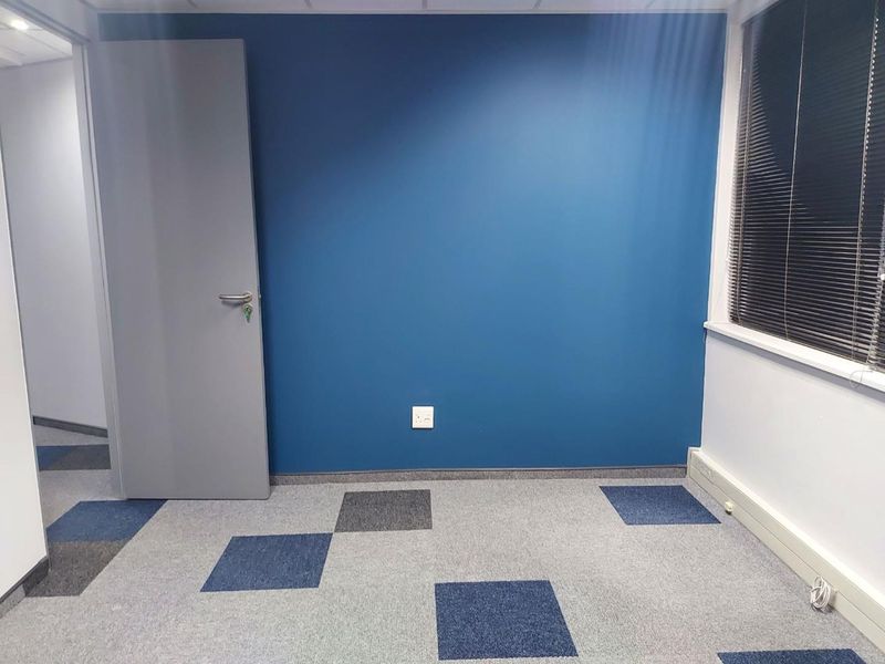 A clean, empty office space featuring blue accent wall, grey carpet tiles, and venetian blinds, providing a professional environment ready for occupancy.