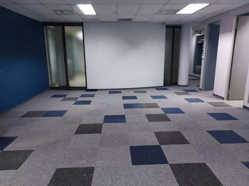 A spacious, empty office area featuring modern carpet tiles, suspended ceilings with recessed lighting, and frosted glass partitions for a professional workspace.
