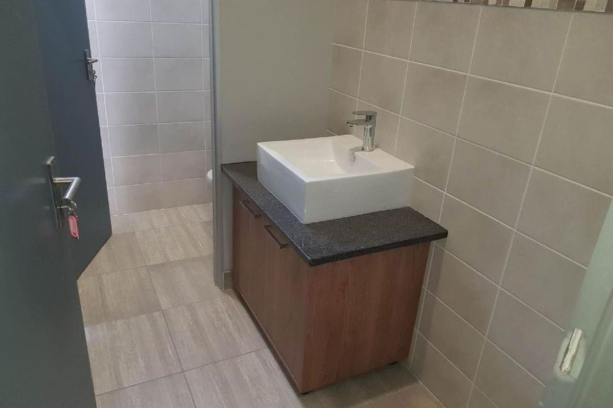 A clean office restroom featuring a modern vessel sink, vanity cabinet, and neutral wall tiling.