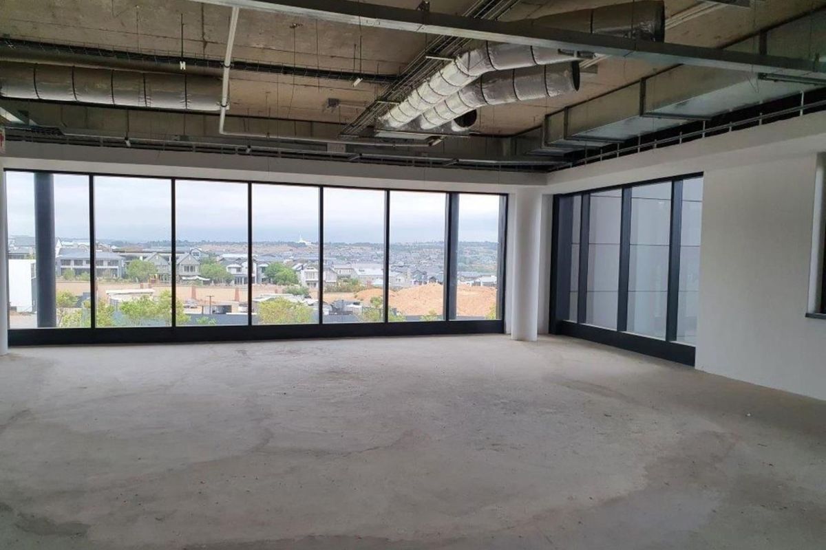 An expansive, open-plan office space in shell condition, featuring exposed industrial ceilings, concrete flooring, and large windows offering panoramic views.