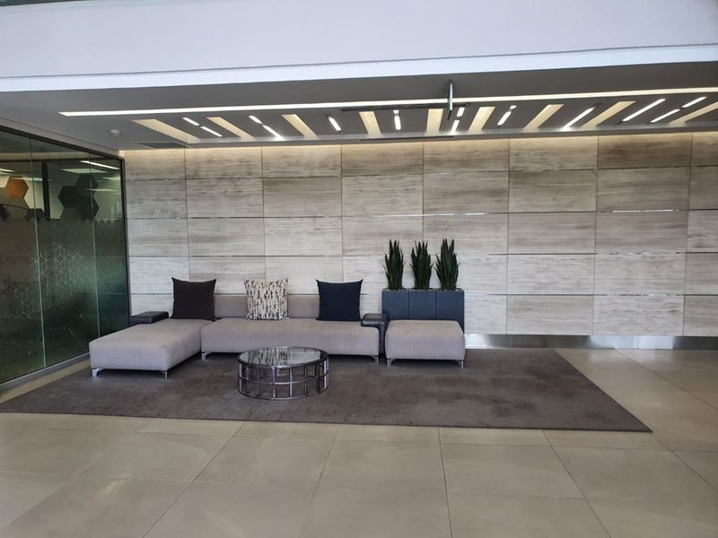 Modern office reception area featuring high-end stone wall cladding, recessed linear ceiling lighting, and sleek glass partitioning.