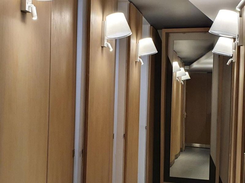 A modern office hallway featuring wood-paneled walls, integrated cabinetry, wall-mounted lighting, and a large full-length mirror.