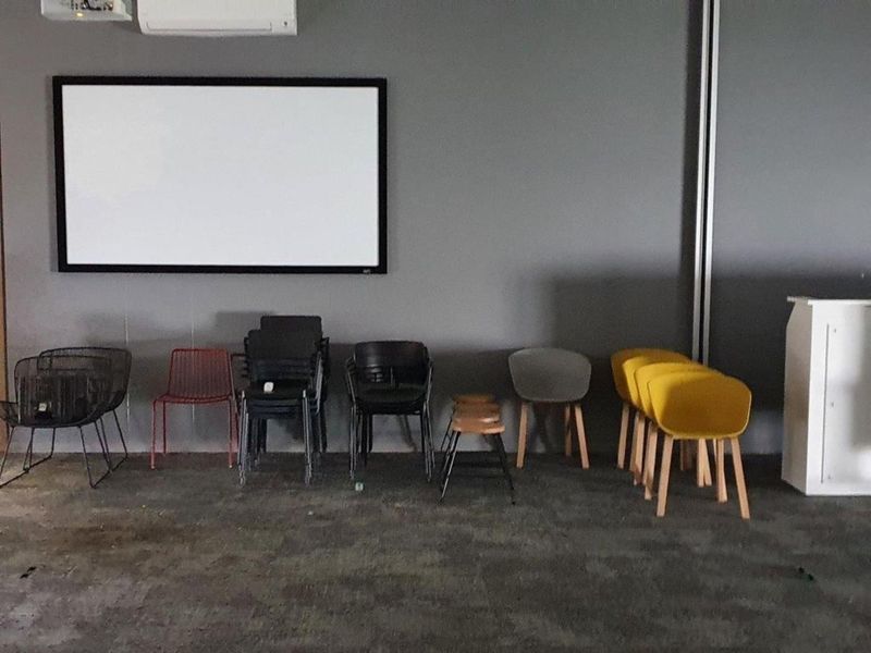 Office space featuring a wall-mounted projector screen and air conditioning unit, with visible wear on the flooring.