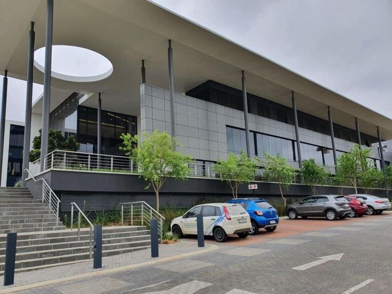 Modern office building exterior featuring a prominent cantilevered roof, glass facade, metal paneling, and a structured concrete staircase leading to the entrance.