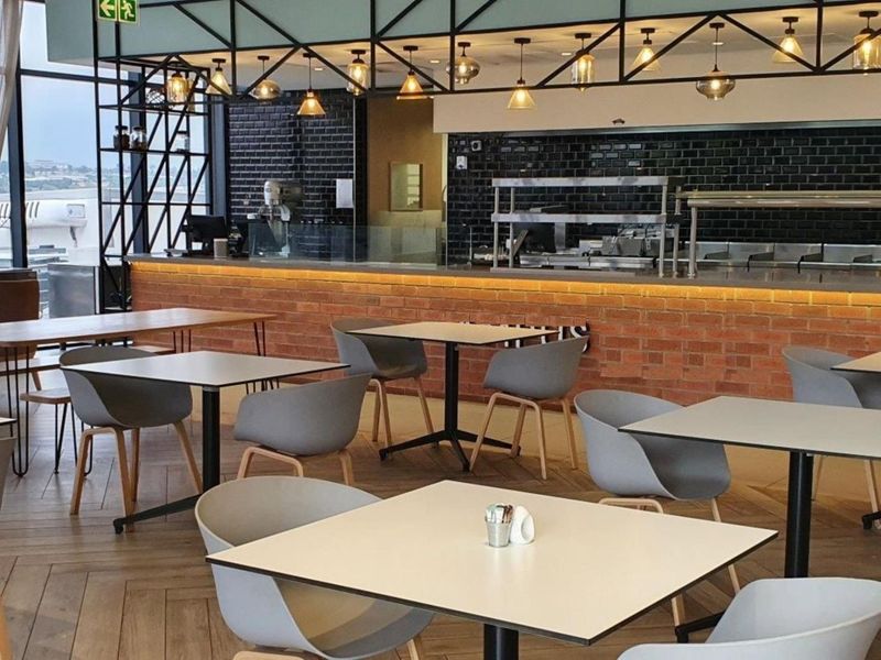 Modern open-plan office break area featuring industrial design elements, exposed brick counters, subway tile backsplashes, and large windows with natural light.