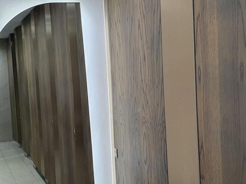 A clean, modern office hallway featuring floor-to-ceiling wood-finish built-in cabinetry and neutral tiled flooring.