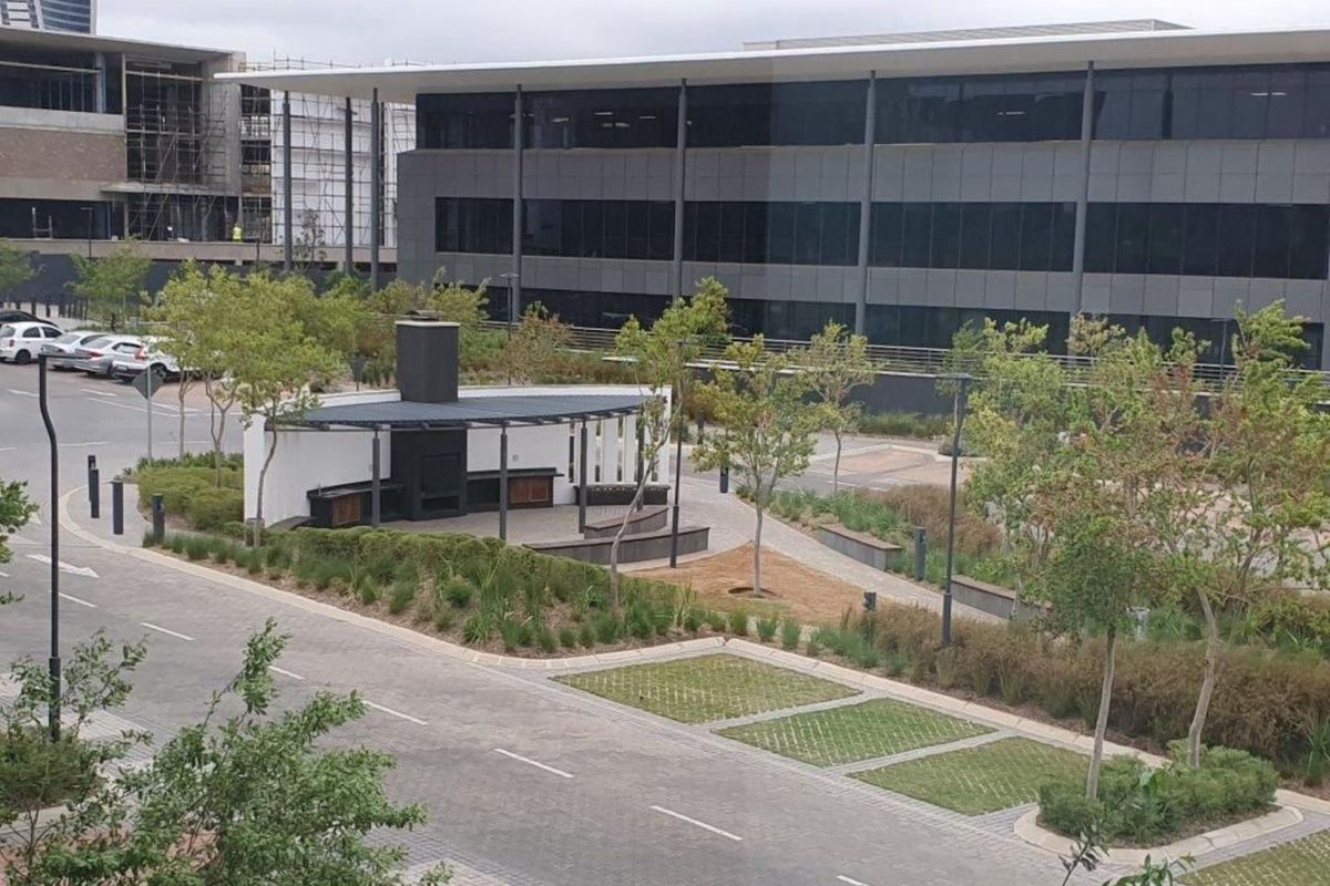 An elevated view of a modern outdoor entertainment area featuring a covered patio with a built-in braai, surrounded by landscaped gardens and paved pathways.