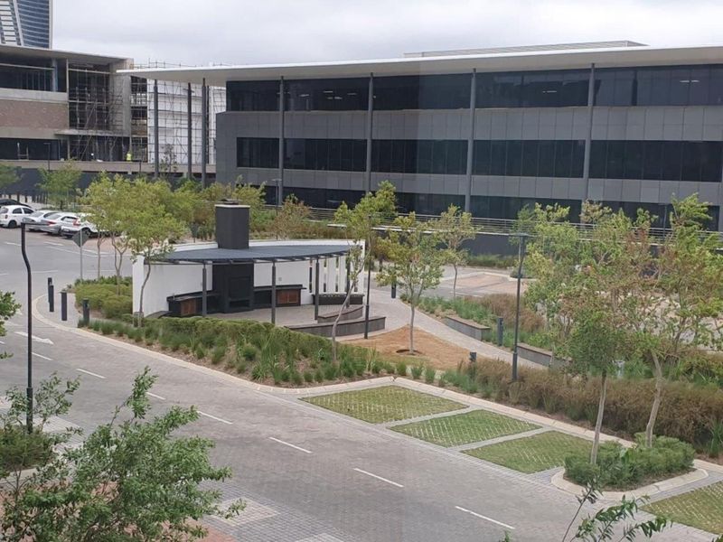 An elevated view of a modern outdoor entertainment area featuring a covered patio with a built-in braai, surrounded by landscaped gardens and paved pathways.