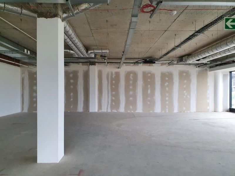 An open-plan office space in shell condition, featuring exposed concrete ceilings, industrial HVAC ducting, and unfinished drywall partitions ready for final fit-out.