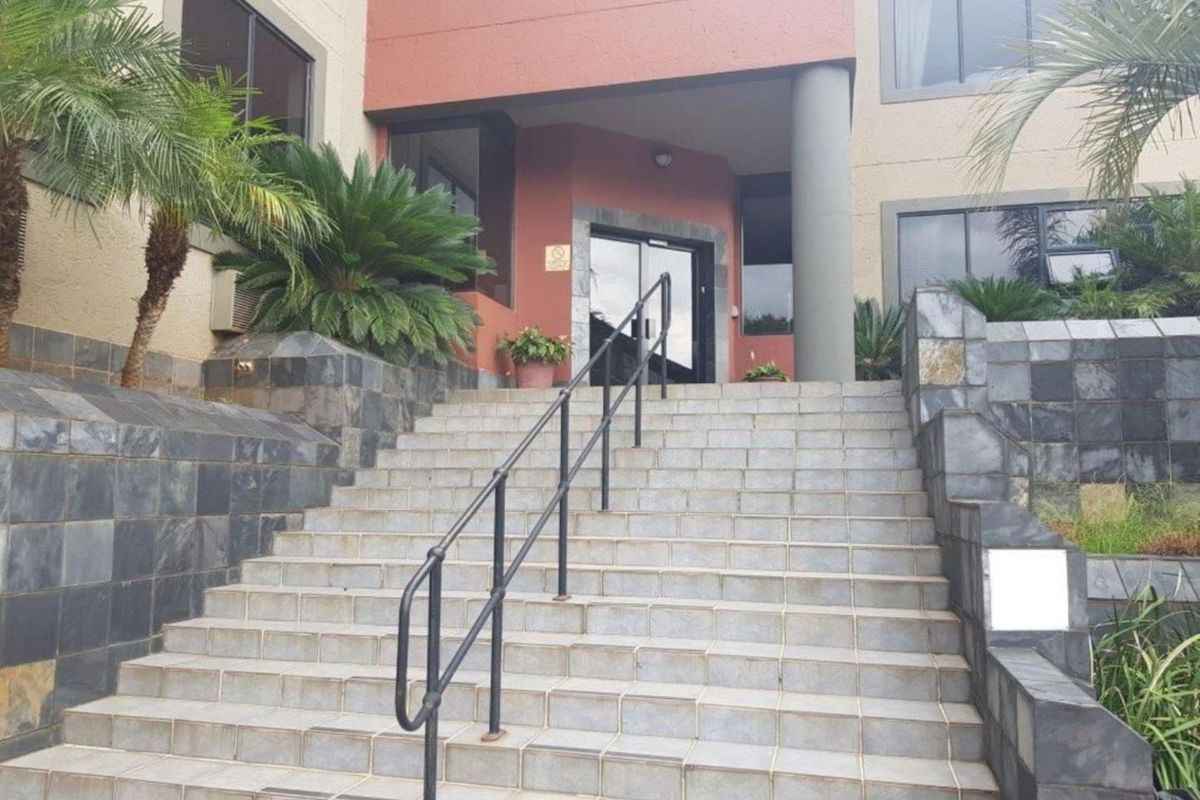 Front entrance of the office building featuring a wide tiled staircase with metal handrails and stone-clad retaining walls.