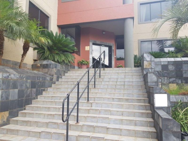 Front entrance of the office building featuring a wide tiled staircase with metal handrails and stone-clad retaining walls.