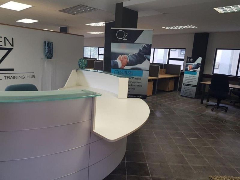 A professional office space featuring a modern reception desk, tiled flooring, partitioned workstations, and recessed lighting in a suspended ceiling.