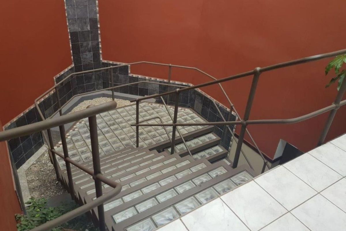 An outdoor staircase featuring metal handrails and unique glass block treads, leading down to a small gravel landing with a tiled feature wall.