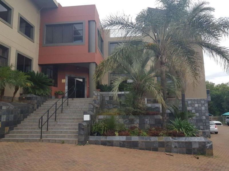 Front elevation of a multi-story office building featuring stone-clad retaining walls, a paved driveway, and a prominent concrete staircase leading to the main entrance.