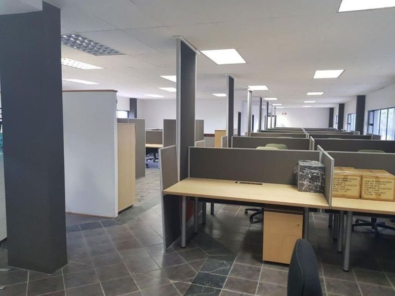 Open-plan office space featuring built-in cubicle partitions, suspended ceilings with recessed lighting, and durable tiled flooring throughout.