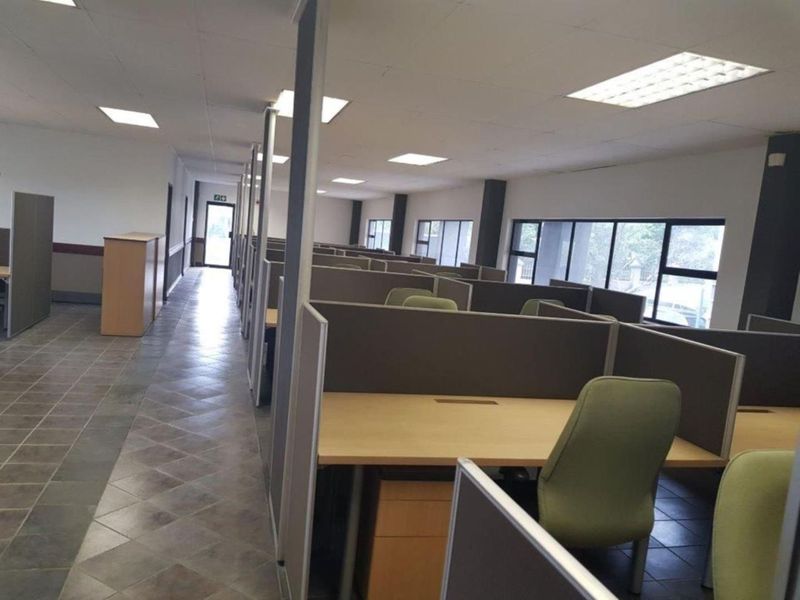 Open-plan office space featuring multiple built-in cubicle workstations, large windows for natural light, and tiled flooring throughout.