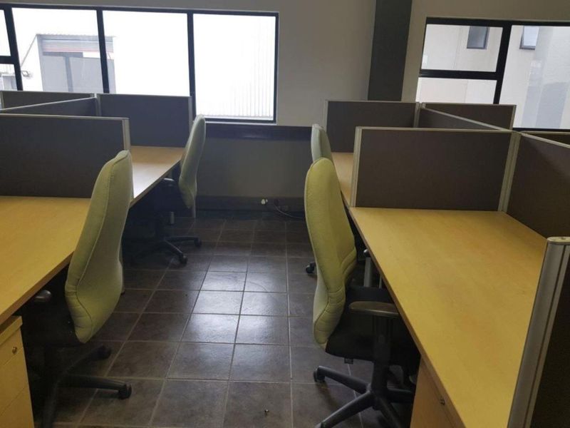 Functional office space featuring built-in cubicle workstations, tiled flooring, and large windows providing natural light.