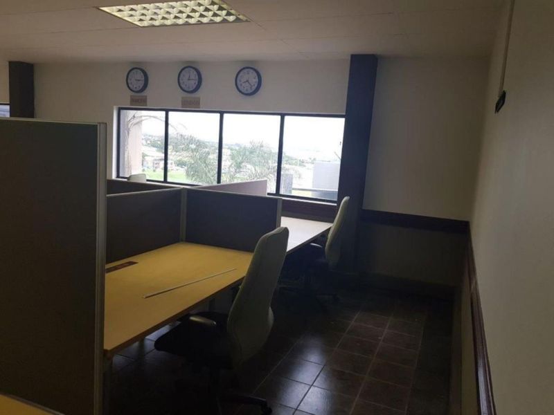 An office space featuring built-in cubicle partitions, tiled flooring, and a large window providing natural light and exterior views.
