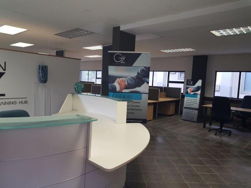 Open-plan office space featuring a reception area, partitioned workstations, tiled flooring, and recessed ceiling lighting.