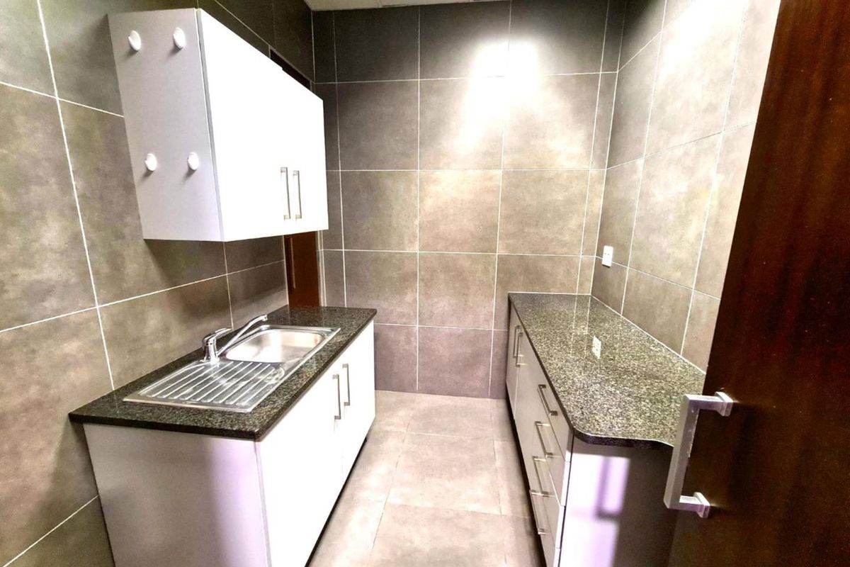 A compact office kitchenette featuring granite countertops, stainless steel sink, and modern cabinetry with full-height wall tiling.